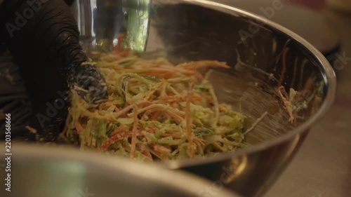 Chef mixing fresh shredded cabbage and carrot salad in a stainless steel bowl in a commercial restaurant kitchen, close-up food preparation.