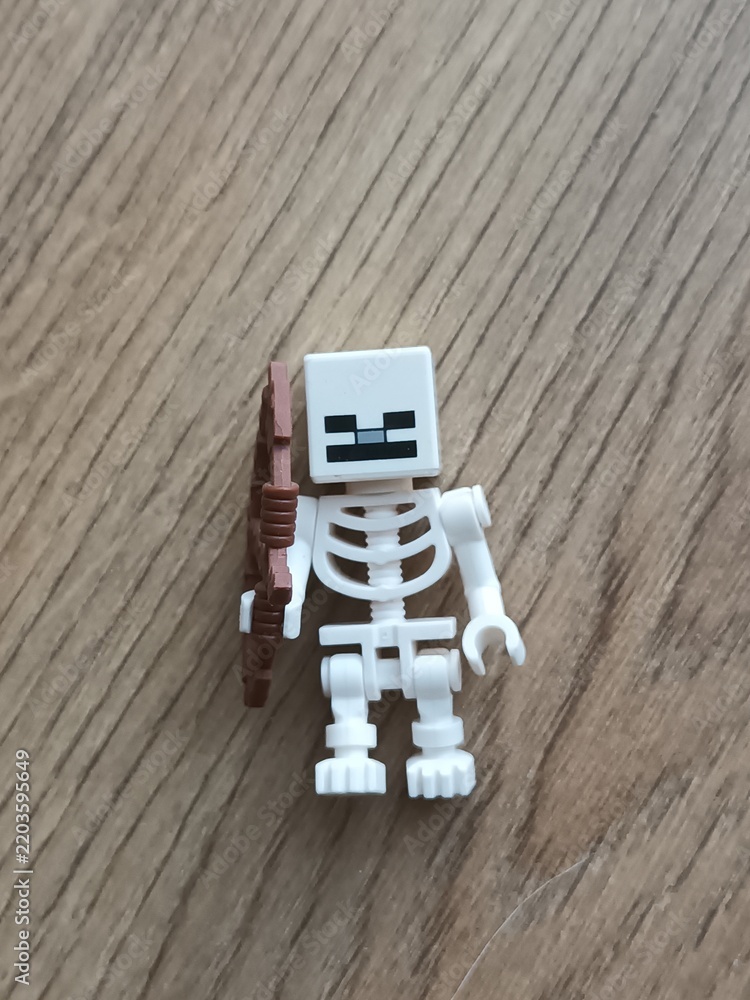 Fototapeta premium A white Lego Minecraft skeleton minifigure holding a brown plastic bow on a wooden surface