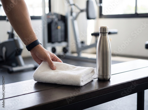 Hand placing a towel beside a water bottle in a gym setting  