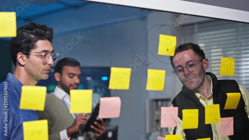 Business Team Brainstorming Ideas on Glass Wall with Sticky Notes
