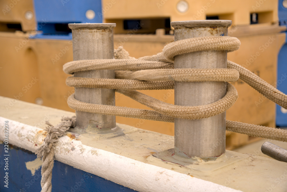 Fototapeta premium Mooring rope wrapped around a steel double bitt deck cleat on a ship in Rijeka harbor, Croatia. Vessel deck hardware detail.