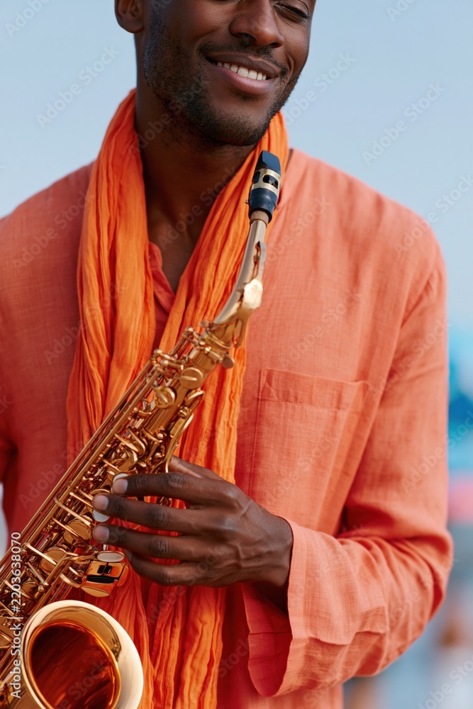 Fototapeta premium Stylish male saxophonist wearing an orange scarf playing a golden saxophone outdoors for music poster and portrait banner