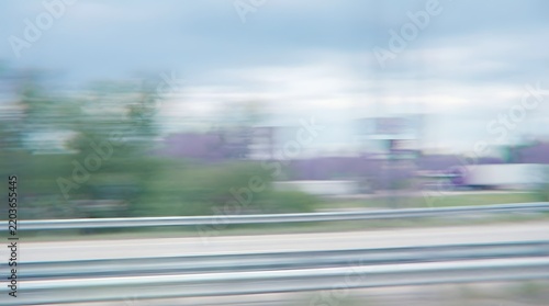 A blurry landscape shot capturing trees and buildings with a motion blur effect, suggesting movement or speed