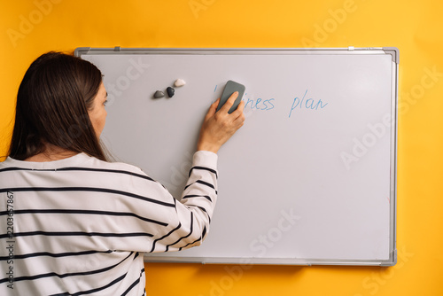 Woman erasing Business plan from a whiteboard with a gray eraser.