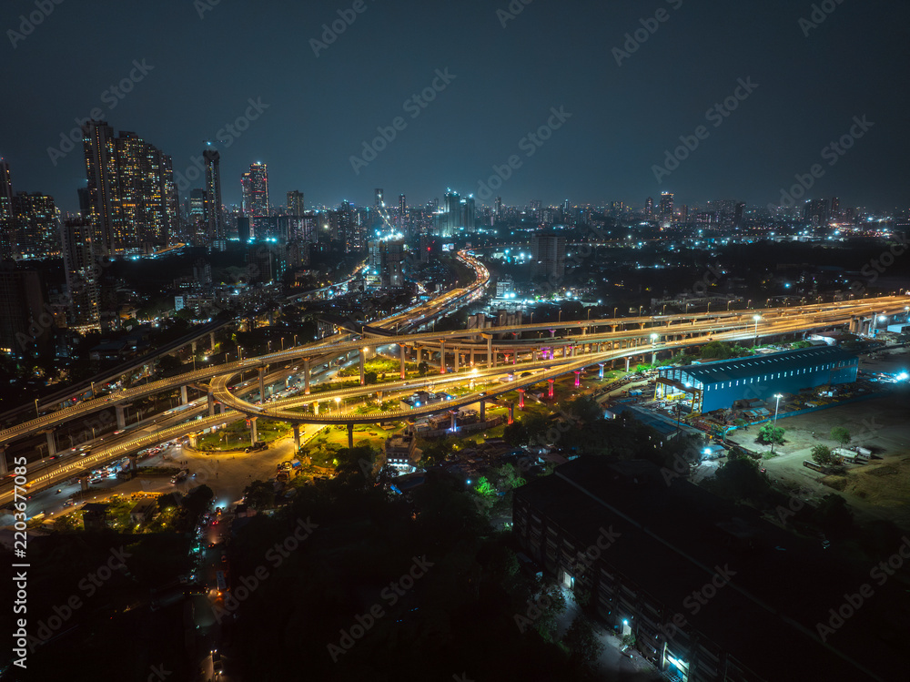 Fototapeta premium A stunning aerial night view of Atal Setu (Mumbai Trans Harbour Link), showcasing the intricate network of illuminated flyovers and highways glowing in golden light.