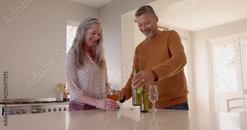 Sharing laughter and conversation, senior couple drinking wine in modern kitchen together