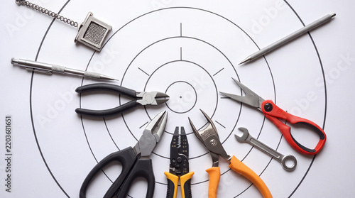 Collection of hand tools including pliers, scissors, and wire strippers arranged on a white bullseye target background, representing precision, repair goals, and professional craftsmanship.