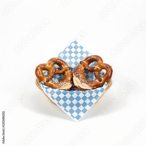 Two salted brown pretzels in a wicker basket with a blue and white checkered napkin background