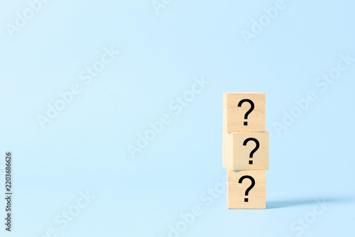 Three stacked wooden blocks with question marks on a blue background represent uncertainty, questions, problem solving, decision making, curiosity, confusion, inquiry, challenge, and seeking answers.