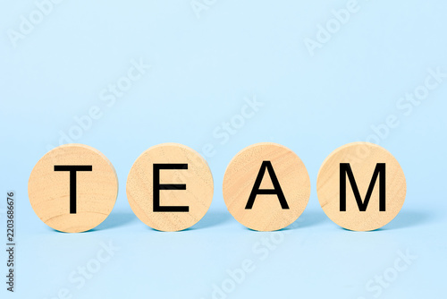 Wooden round blocks spelling team on a blue background represent teamwork, collaboration, partnership, unity, leadership, cooperation, organization, employee engagement, and business success.