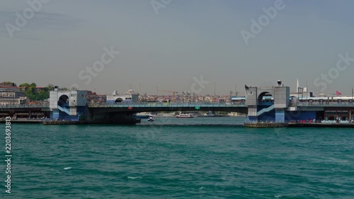 Panoramic view of the historic Galata bridge in Istanbul over the turquoise water of the Golden Horn during a bright sunny day with city buildings in background
