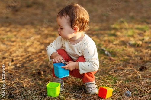 Toddler playing with colorful cups and pinecone outdoors