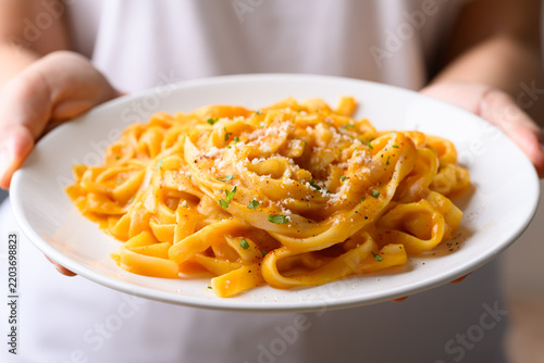 Butternut squash pasta topped with grated parmesan cheese and fresh herbs on white plate holding by woman hand, Autumn seasonal food