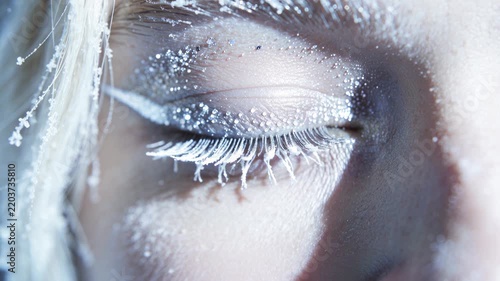Slow motion shot Blue eyes, adorned with snowflakes and frost, accentuate the look, creating a festive mood, fantasy, and a wintery theme, creating a charming beauty