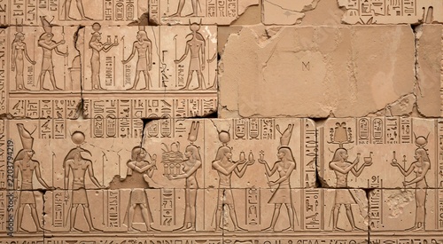 Ancient Egyptian hieroglyphics carved on cracked stone wall relief. Historical temple carvings with gods and pharaoh figures