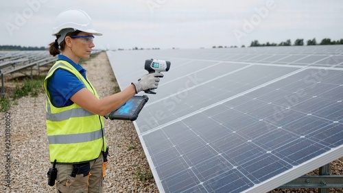 Solar technician scans photovoltaic panels with handheld thermal camera, revealing bright heat patterns during inspection at a large outdoor solar power facility