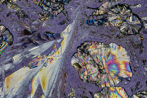 Polarized light microscopy of homegrown chemical crystals showing large disc like spherulites and sharp wedge shaped structures on textured lavender purple background for chemistry science abstract
