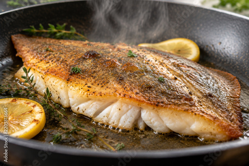 Cooked fish fillet in a frying pan, crispy golden skin and flaky white flesh.