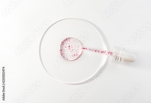 Glass pipette containing a clear liquid with suspended red particles, hovering over a petri dish 