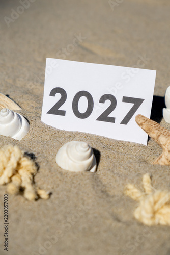 2027 text start new year symbol on paper greeting card on background of starfish summer vacation decor. Sandy beach sun coast. Holiday concept postcard. Getting away Travel Business concept