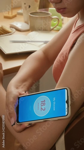 Vertical video of biracial young girl scanning glucose sensor on arm using smartphone and logging data in notebook. Ideal for modern diabetes management, medical technology and healthcare ads