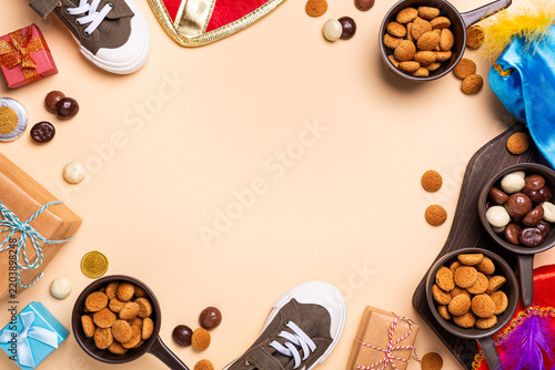 Overhead festive arrangement for Sint Nicholas day, Dutch Sinterklaas shows shoes, wrapped presents, cookies, chocolates, colorful feathers, creating seasonal holiday composition with copy space