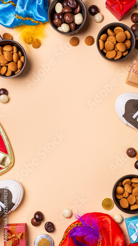 Sinterklaas holiday arrangement features bowls of chocolate and spiced cookies around gifts, shoes on peach surface, top view stories templates with copy space