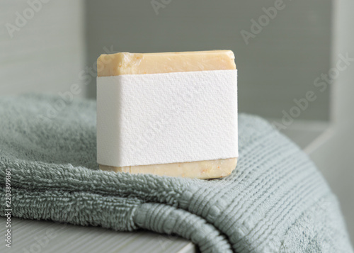 Beige handmade soap mockup with blank label on sage green towel in bathroom, unbranded packaging