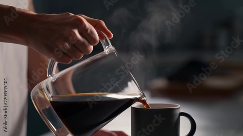 Steam rises as dark coffee pours into a mug. Hands steady, showing care in the pouring motion. Warmth suggests comfort in a quiet moment. Ideal for scenes of morning routines or cozy settings