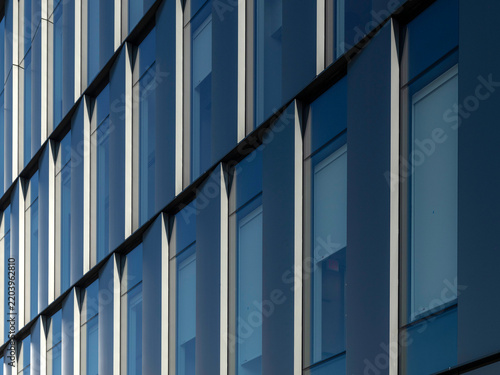 Close-up angled view of a curtain wall facade with repeating glass windows and vertical shading fins, receding diagonally across the frame.