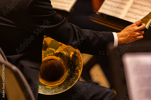 Close up of musician hands holding french horn and turning sheet music page during orchestra performance