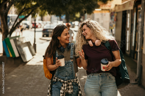 Happy women friends walking city street drinking coffee