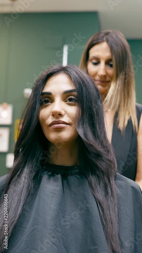 Beautiful smiling customer getting her hair styled by a professional female hairdresser in a modern beauty salon after a haircut. Vertical