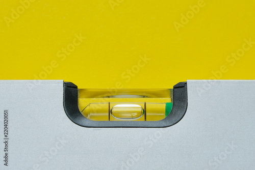 Close-up of grey metal spirit level with bubble against a yellow background. Image with copy space. Balance and stability concept.