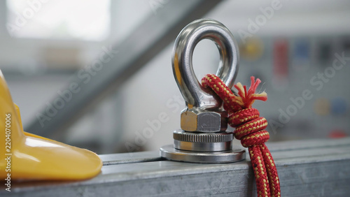 Close-up of a metal eye bolt with red rope and yellow hard hat