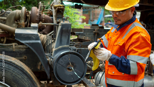 Asian male mechanic wiping dipstick checking engine oil quality in heavy truck.