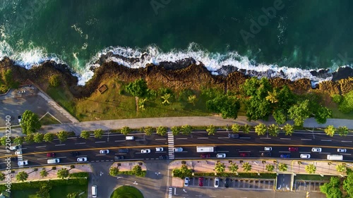 Caribbean Coast Highway and coastal cliffs at sunrise in Santo Domingo. A seaside city, aerial view. Morning city by the ocean. Cars driving along the waterfront road. Waves crashing against the shore