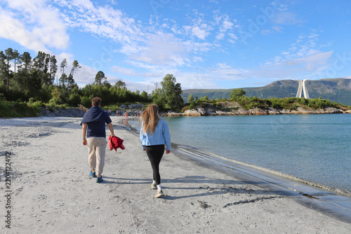 Young couple walking along the white sand beach of Overasanden on Hareid island, Norway. Man and woman enjoying a scenic walk on Overasanden beach with mountains in the background.