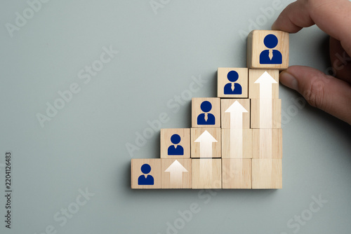 Hand placing wooden block with person icon on step chart with growth arrow for career path and business development concept
