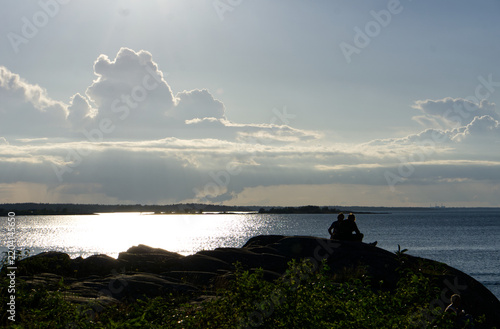 persons sitting on cliff in sunset over the sea
