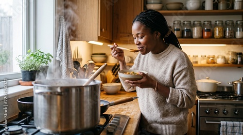 Woman tasting homemade soup from a bowl while cooking in a cozy kitchen