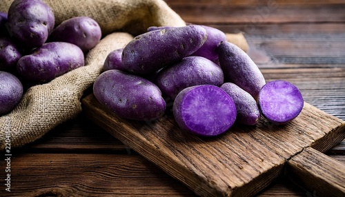raw violet vitelotte potatoes on wooden boards and burlap cloth