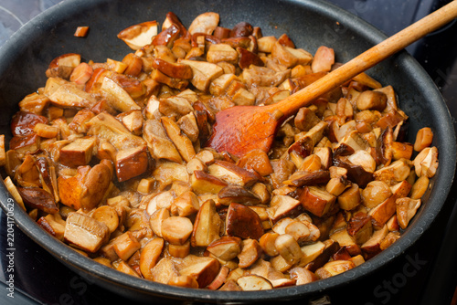 Cooking mushrooms on frying pan with wooden spoon