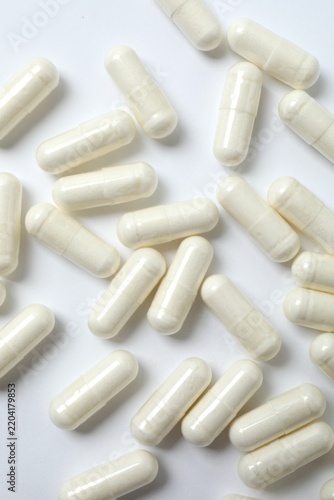 White capsules scattered on white surface, top view. Clean and minimalist medical background