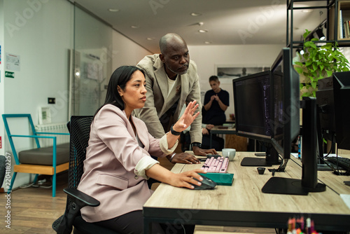 Woman explaining work to colleague at computer in office