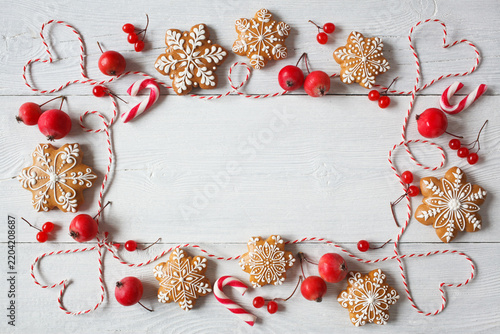 Christmas white wooden background with gingerbread snowflakes,  rope, red apples and berries, space for greeting text, top view.