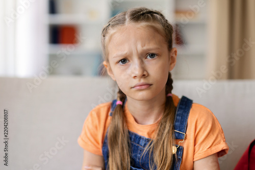 Foto Serious teen girl sitting at home with worried expression, looking toward the ca