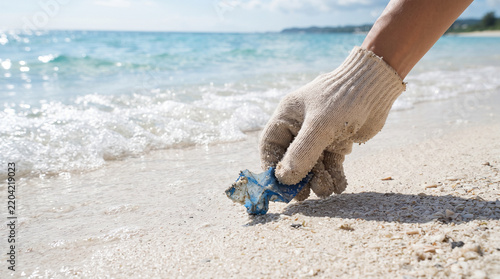 Cleaning the Pristine Shore: A gloved hand carefully picks up a piece of debris from a pristine sandy beach, with gentle waves lapping at the shore.