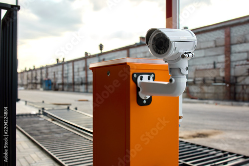 White dome security camera mounted on orange access control post overlooking industrial loading dock area at dusk under overcast cloudy sky