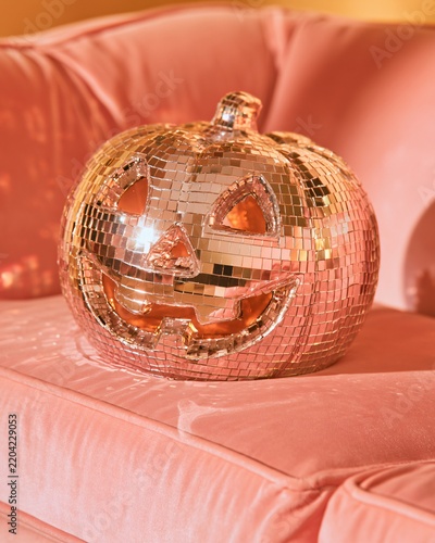 A disco ball pumpkin sits on a pink couch, adding to the Halloween vibe